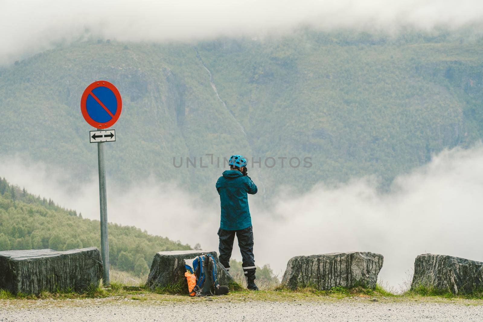 Man in helmet photographer taking photos back view of mountains landscape in rainy weather in Norway. Travel Lifestyle. Wanderlust adventure concept vacations outdoor into the wild.