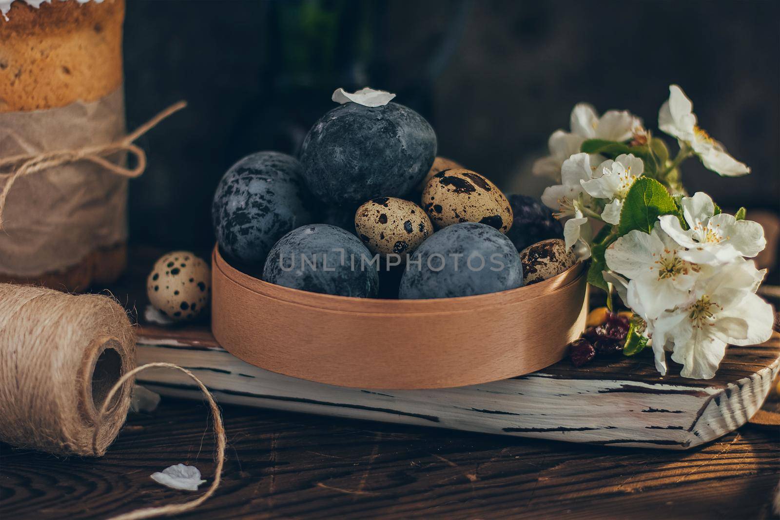 Easter eggs in the round wooden box on rustic wooden background with apple blossom branch