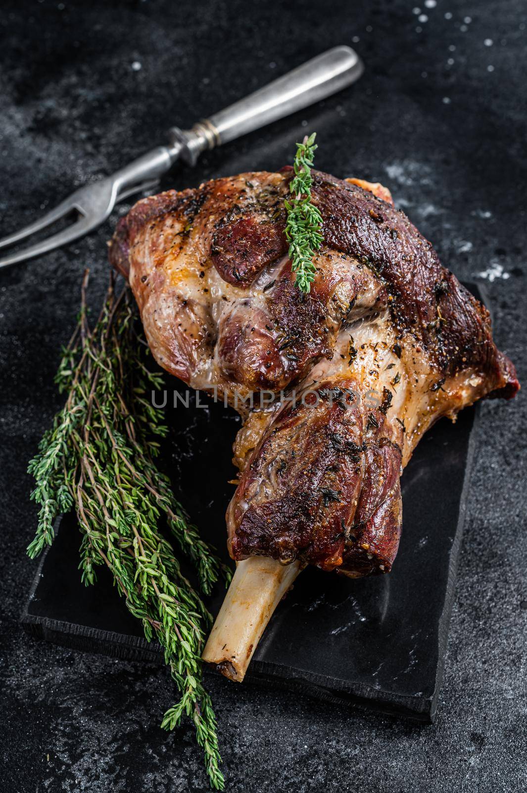 Oven Roasted lamb mutton whole leg with thyme. Black background. Top view.