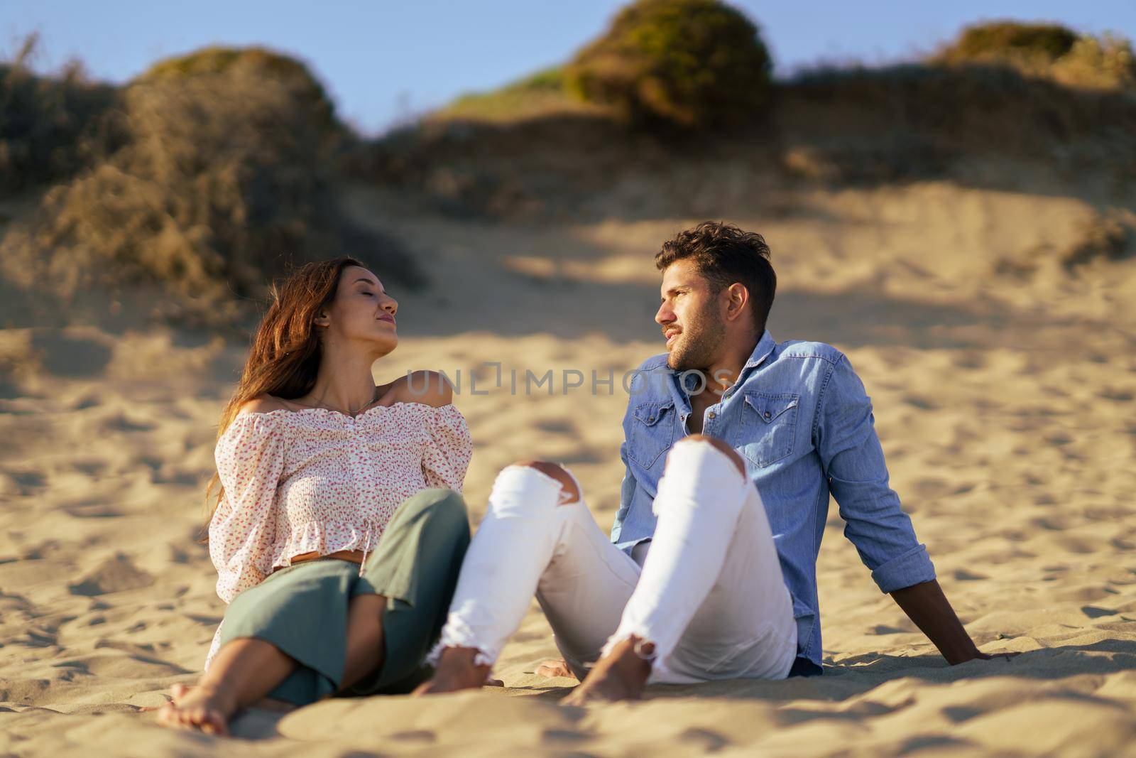 Happy loving couple sitting on the sand of the beach enjoying the tranquility