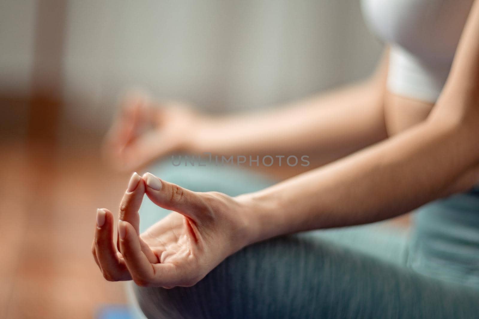 A young woman fitness instructor in violet Sportswear Leggings and Top stretching in the gym before her pilates, on a yoga mat near the large window on a sunny day, female fitness yoga routine concept by panophotograph