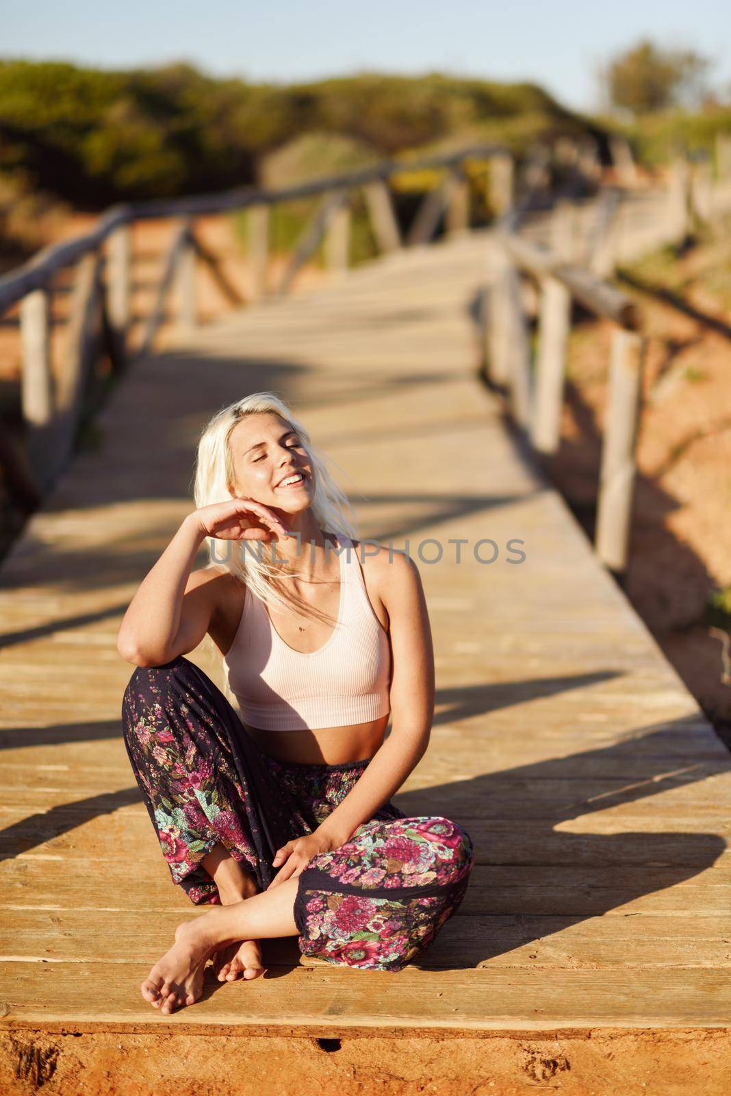 Woman enjoying the sunset on a beautiful beach in Cadiz, Andalusia, Spain. Young female smiling sitting on wooden bridge.