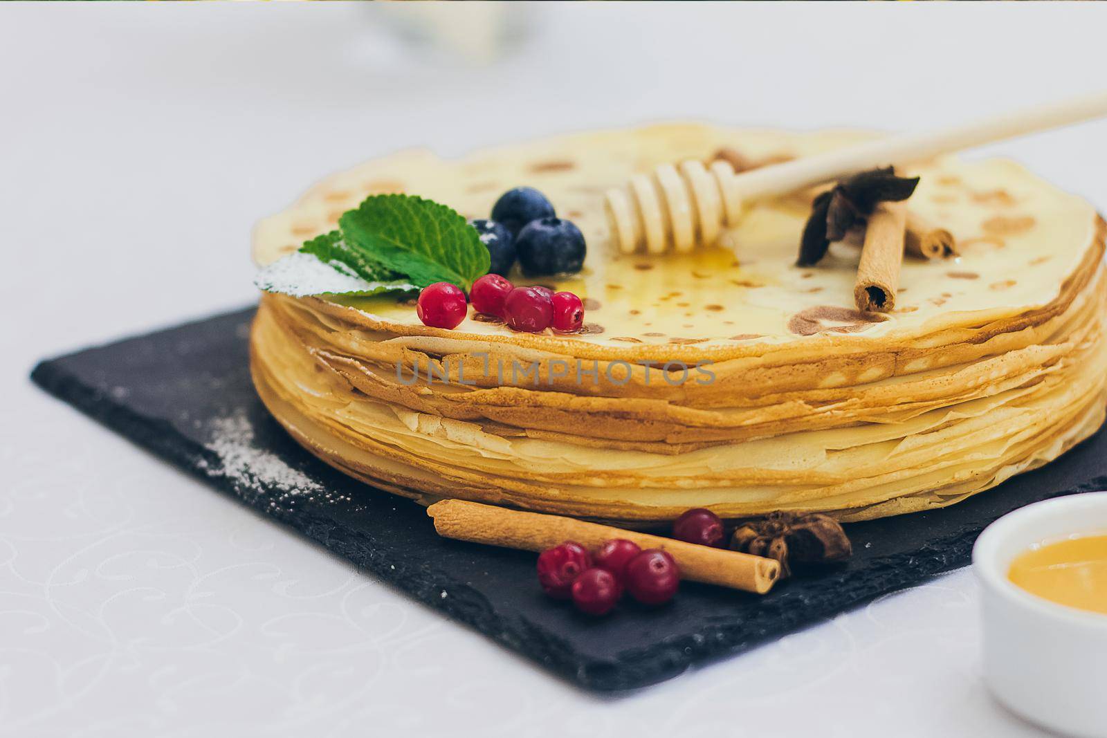 Plate of pancakes dripping with honey with cranberries and blueberries, cinnamon sticks. Shrovetide Maslenitsa Butter Week festival meal. Shrove Tuesday. Pancake day.