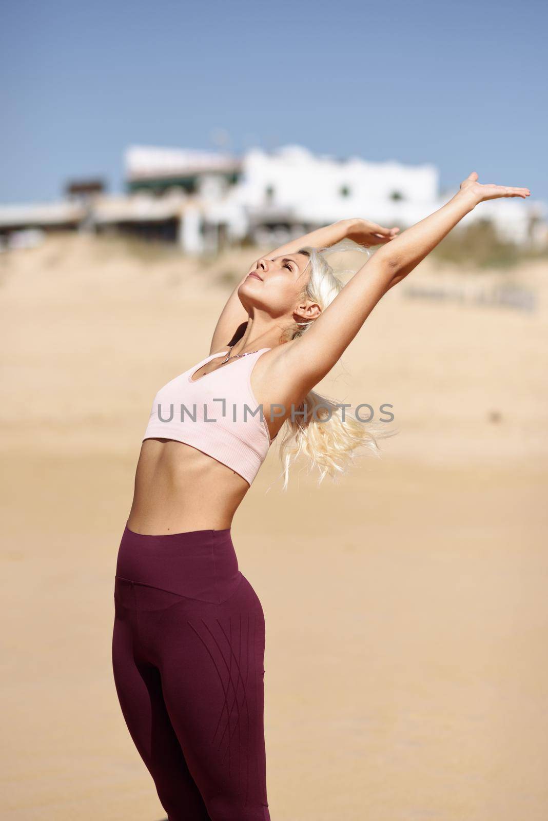 Caucasian woman practicing yoga at seashore. Young female raising arms in the beach in Cadiz, Andalusia, Spain.