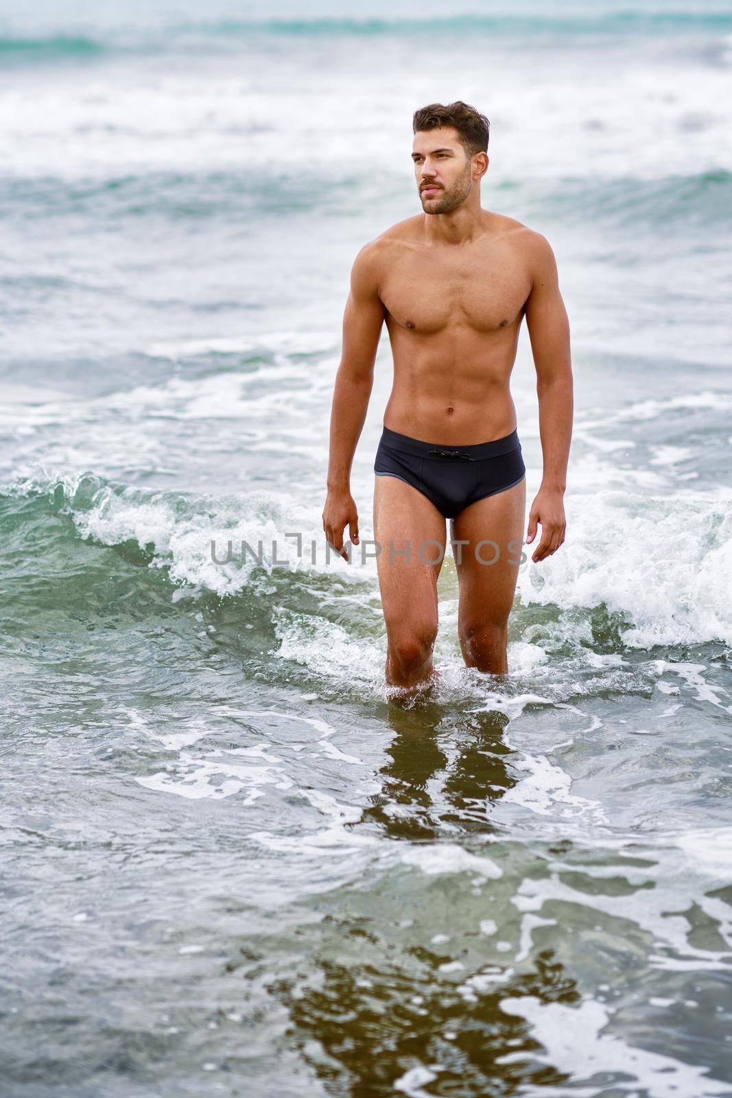 Handsome muscular man bathing on the beach wearing swimwear