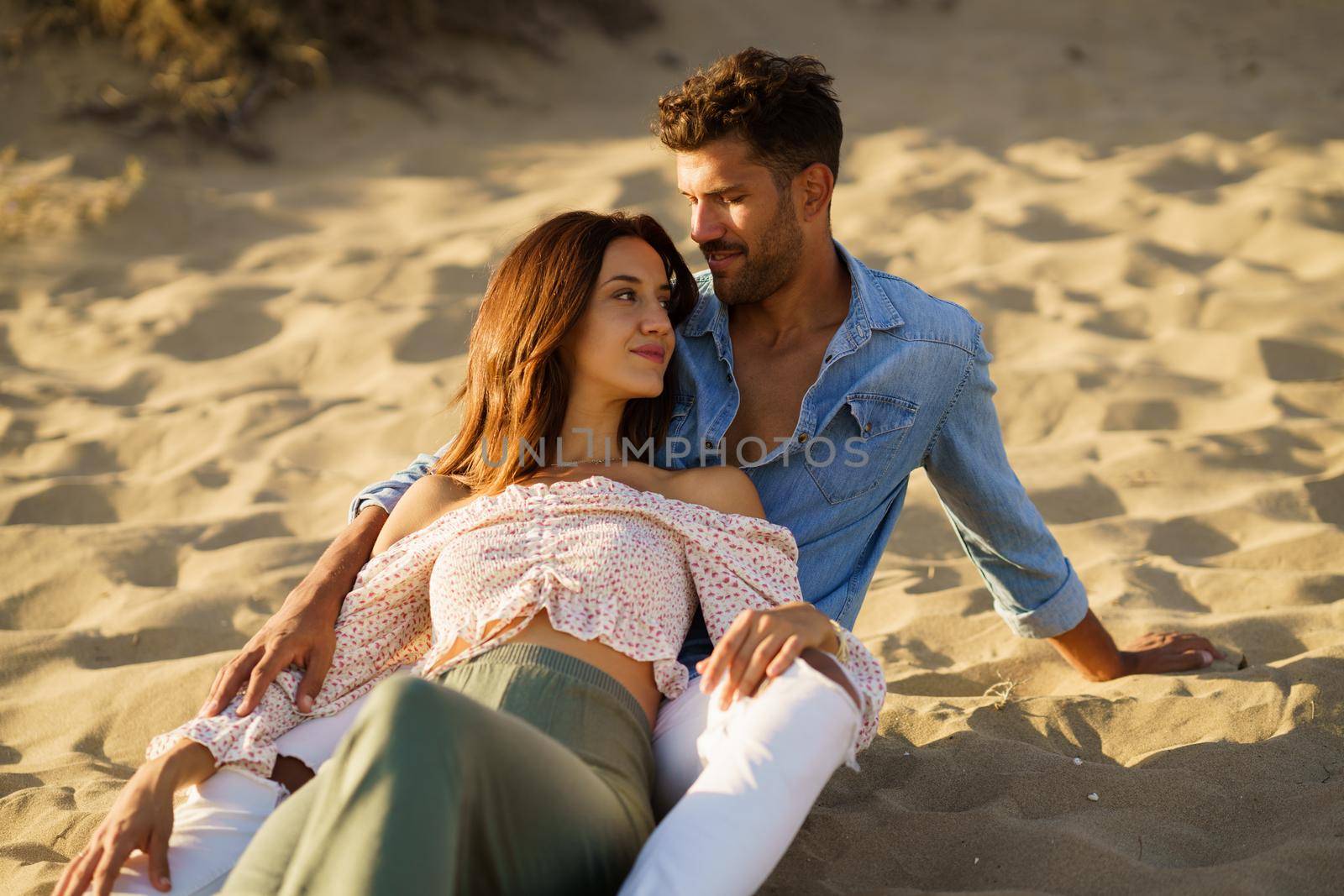 Happy loving couple sitting on the sand of the beach enjoying each other