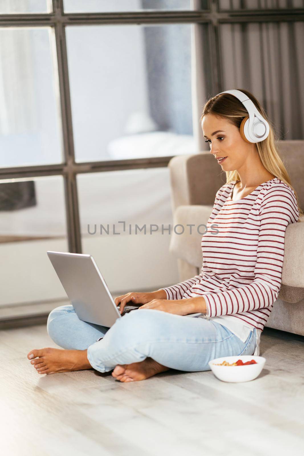 Caucasian blond woman with headphones and laptop on the sofa at home.