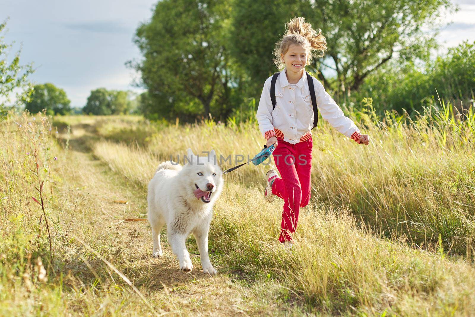 Little girl running with dog in meadow. Child playing with pet in nature, healthy active lifestyle of children, friendship of animals and humans