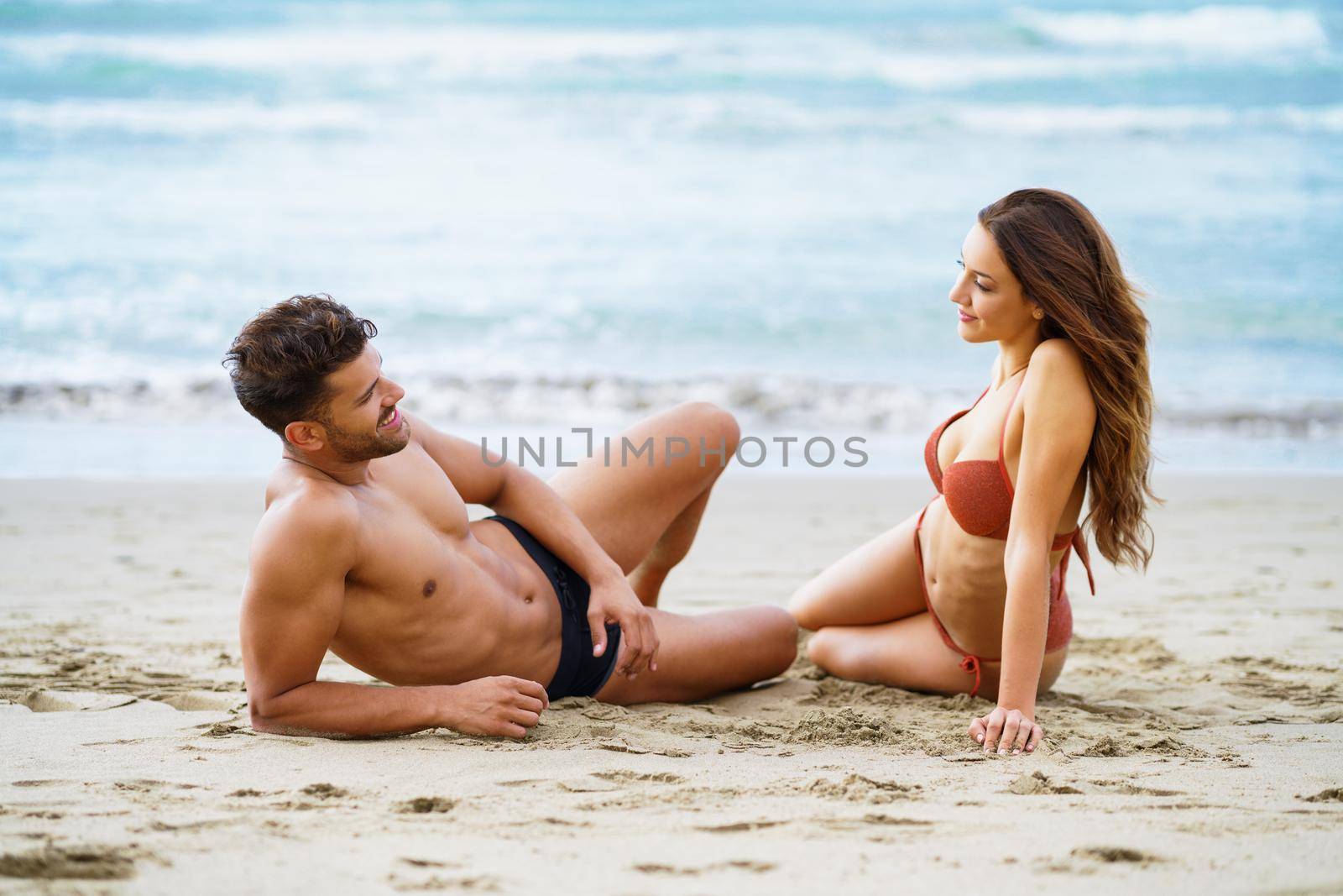 Young couple sitting together on the sand of the beach by javiindy