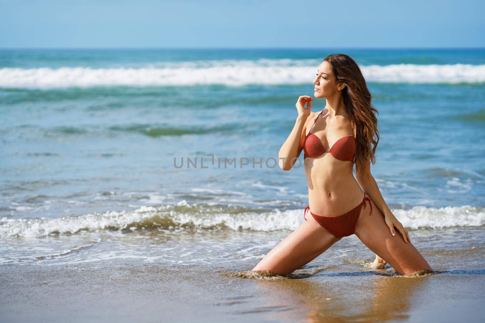 Young woman with beautiful body on her knees on the sand of the beach