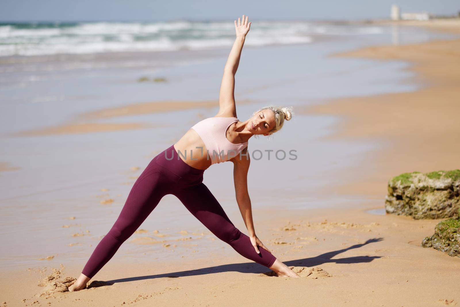 Caucasian blonde woman practicing yoga in the beach by javiindy