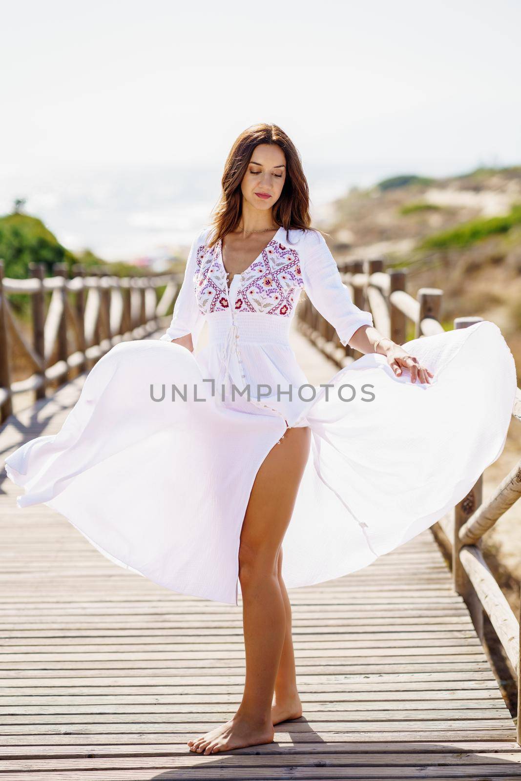 Young pretty woman wearing a beautiful white dress in Spanish fashion on a boardwalk on the beach.