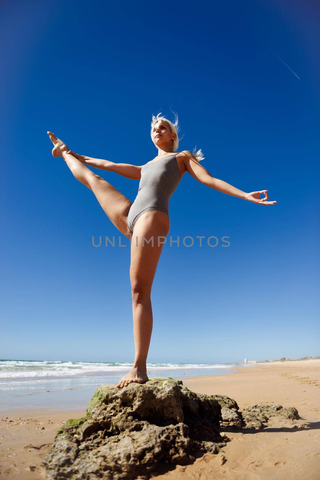 Caucasian woman practicing yoga at seashore. Young female standing on one leg while practicing the tree pose on a tranquil beach in Cadiz, Andalusia, Spain.