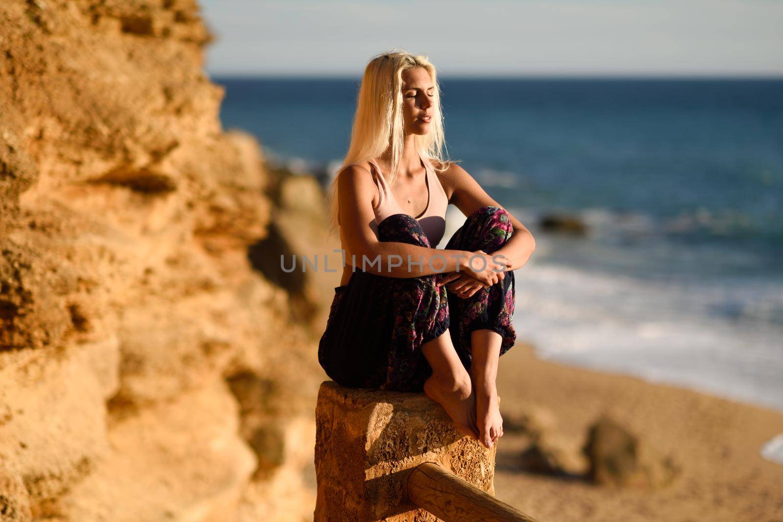 Woman enjoying the sunset on a beautiful beach in Cadiz, Andalusia, Spain. Young female sitting on beautiful stairs looking at the sea with golden light.