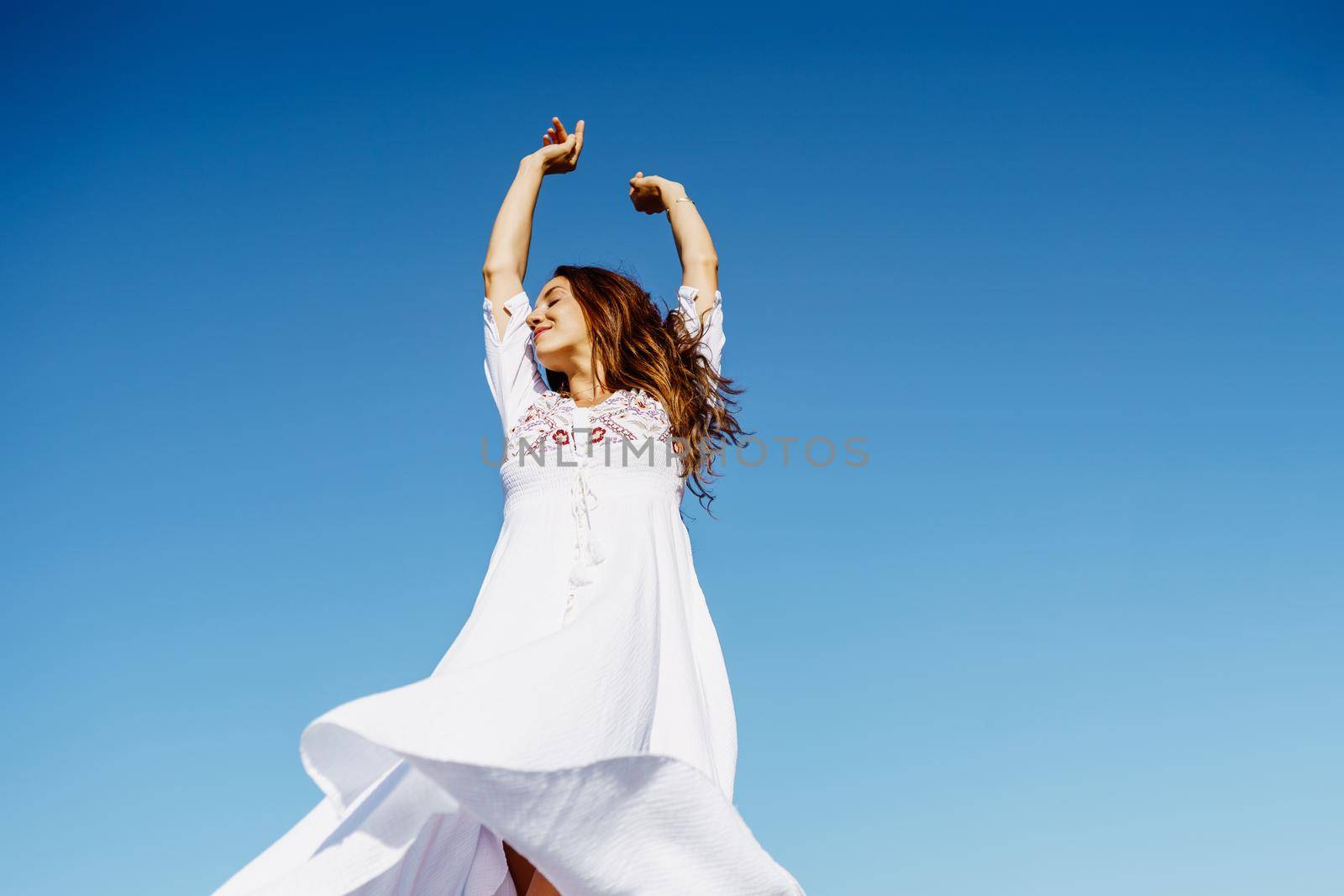 Young beautiful woman raising her arms in a beautiful white dress in Spanish fashion against a blue sky in nature