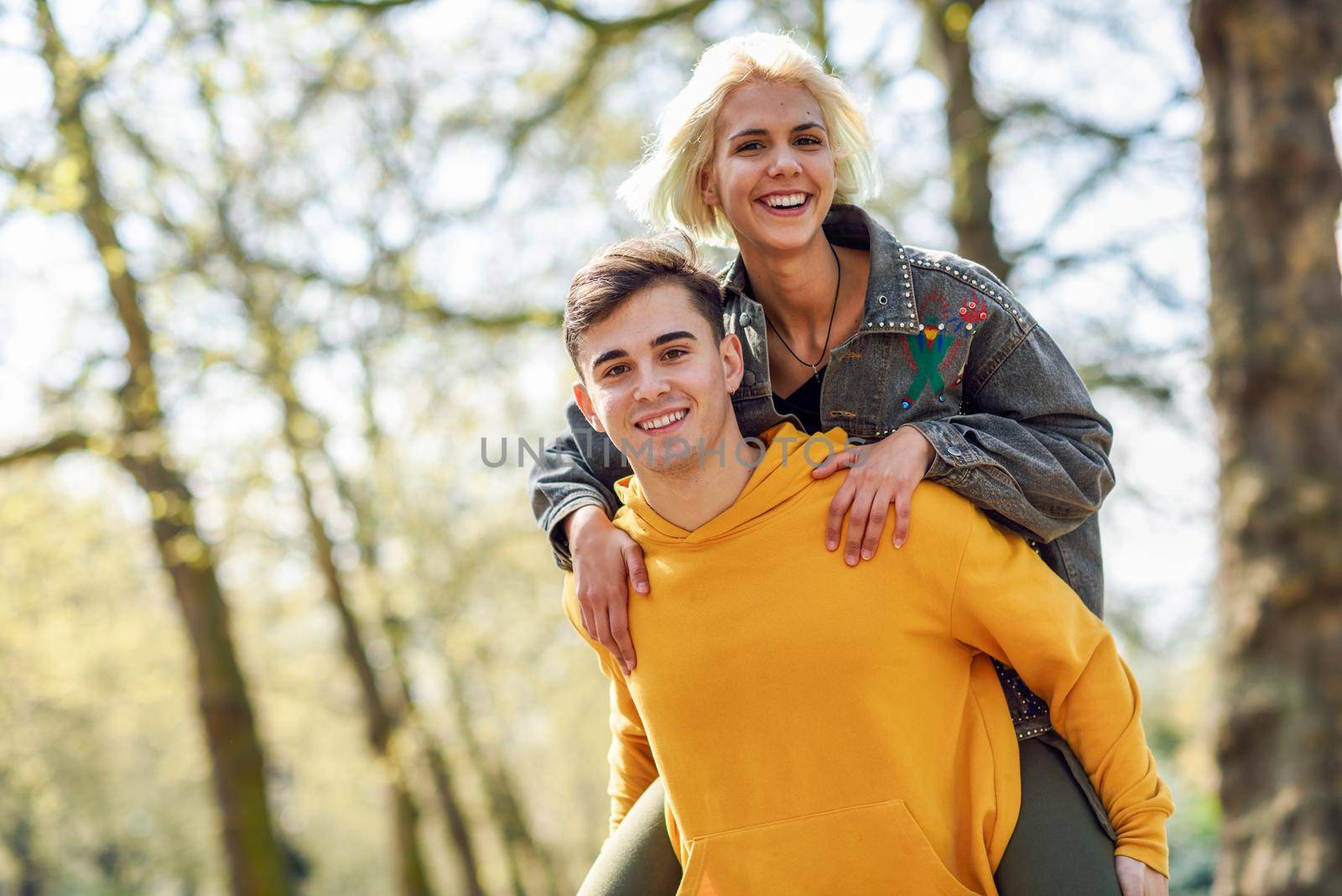 Funny couple in a urban park. Boyfriend carrying his girlfriend on piggyback. Love and tenderness, dating, romance. Lifestyle concept