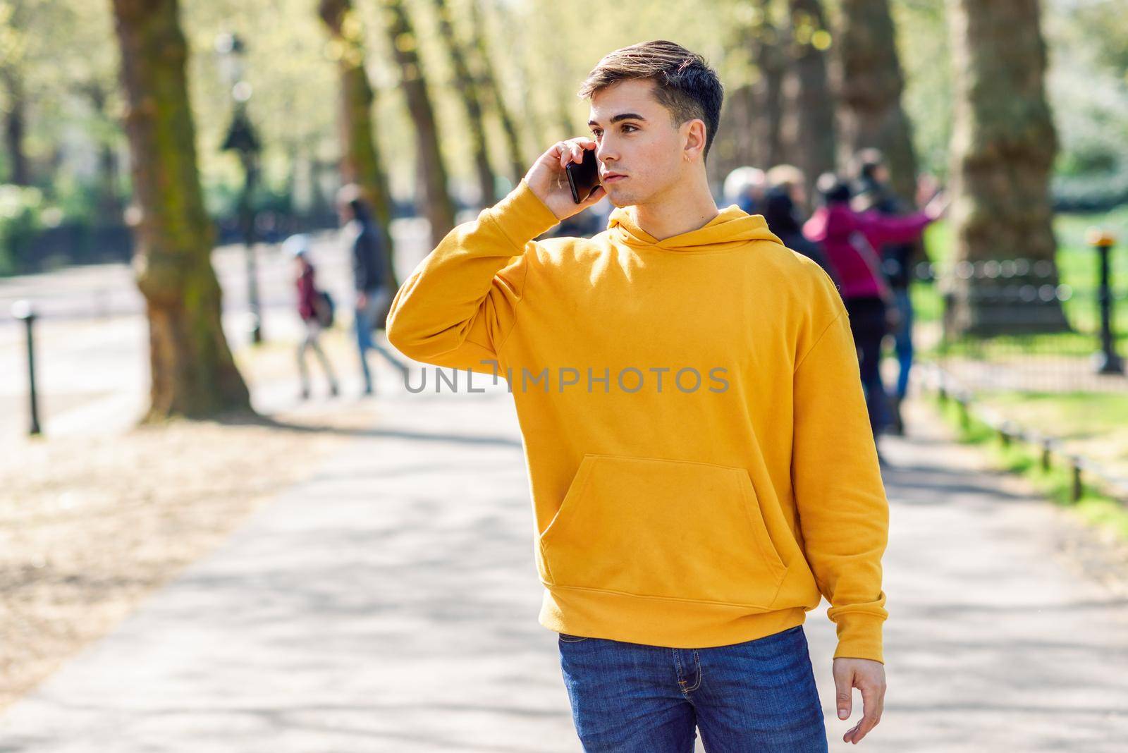 Young urban man using smartphone walking in street in an urban park in London. by javiindy