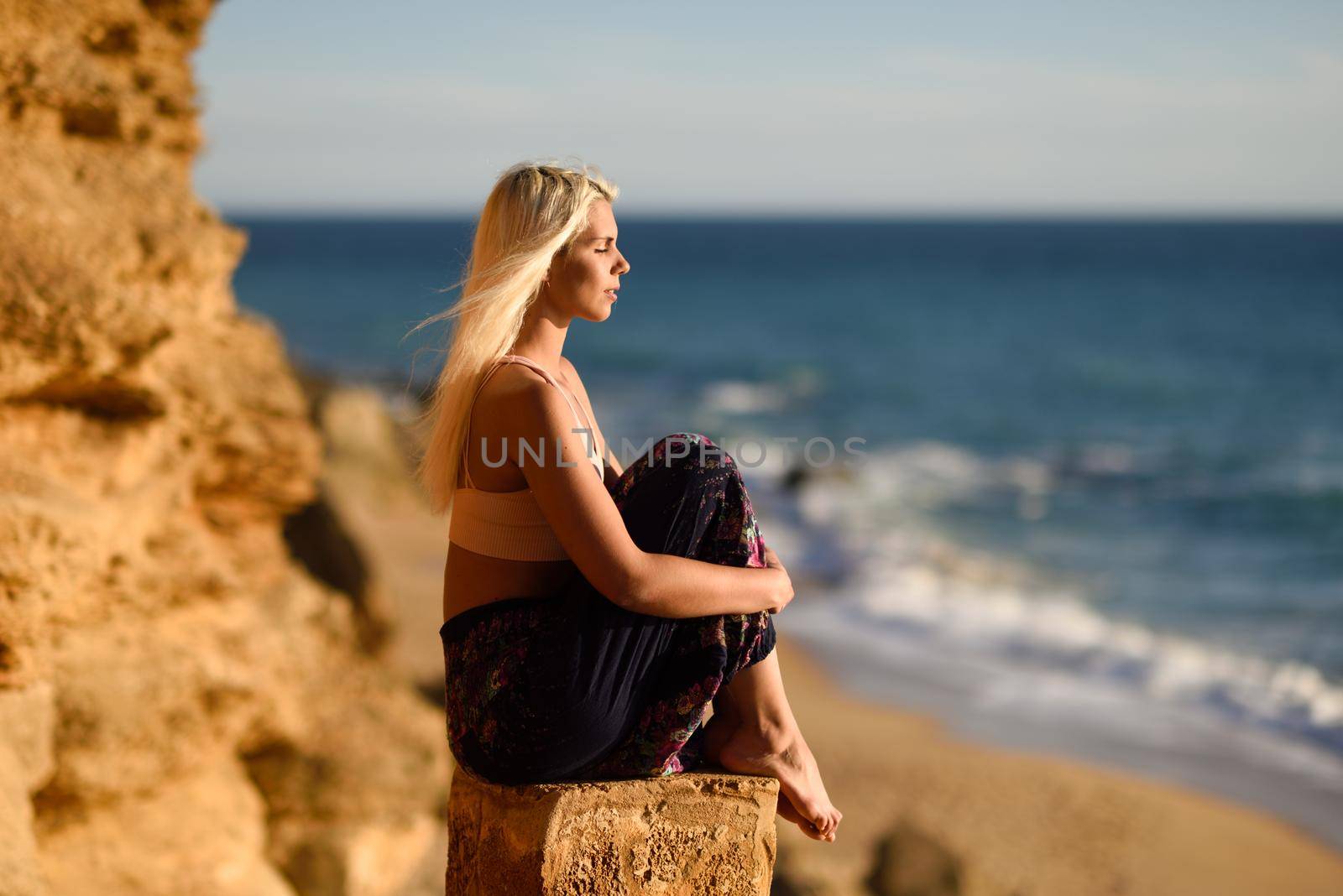 Woman enjoying the sunset on a beautiful beach in Cadiz, Andalusia, Spain. Young female sitting on beautiful stairs looking at the sea with golden light.