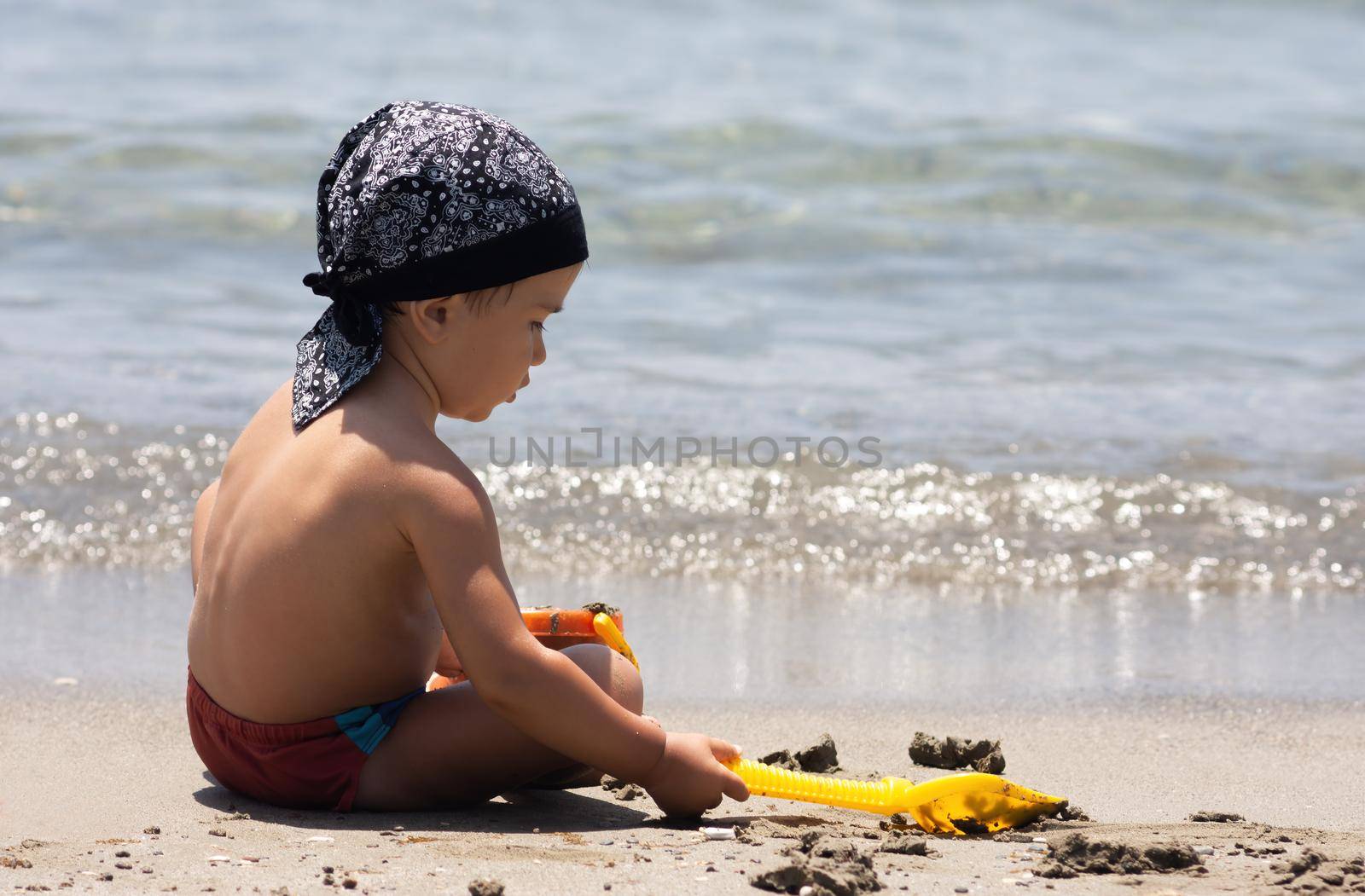 A little boy sits for the first time on the seashore enjoying the fresh air and sea waves