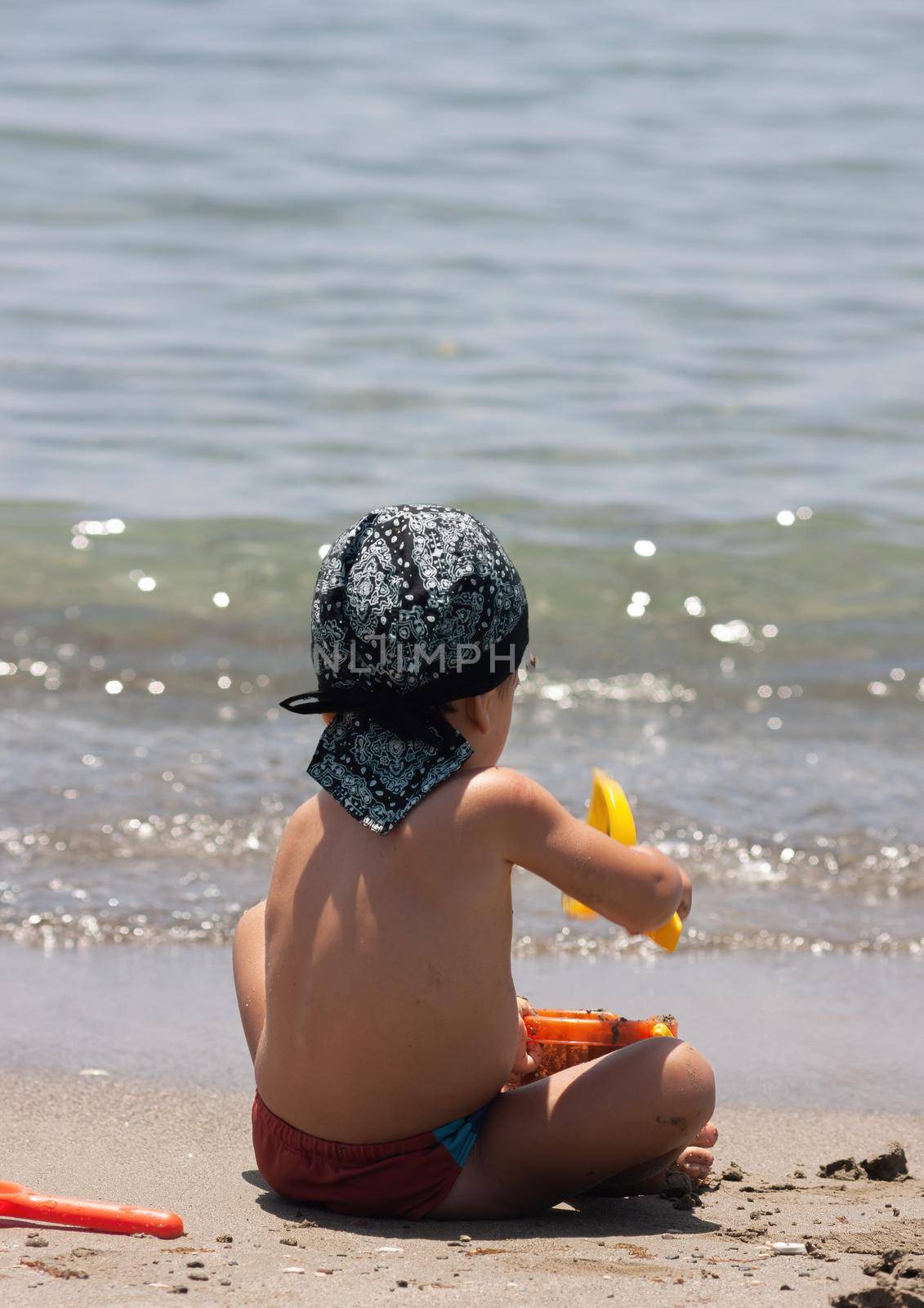 A little boy sits for the first time on the seashore enjoying the fresh air and sea waves