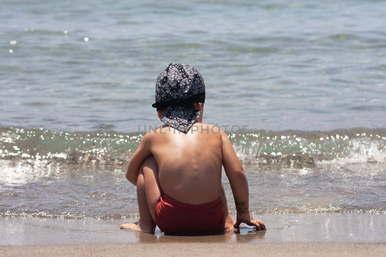 A little boy sits for the first time on the seashore enjoying the fresh air and sea waves