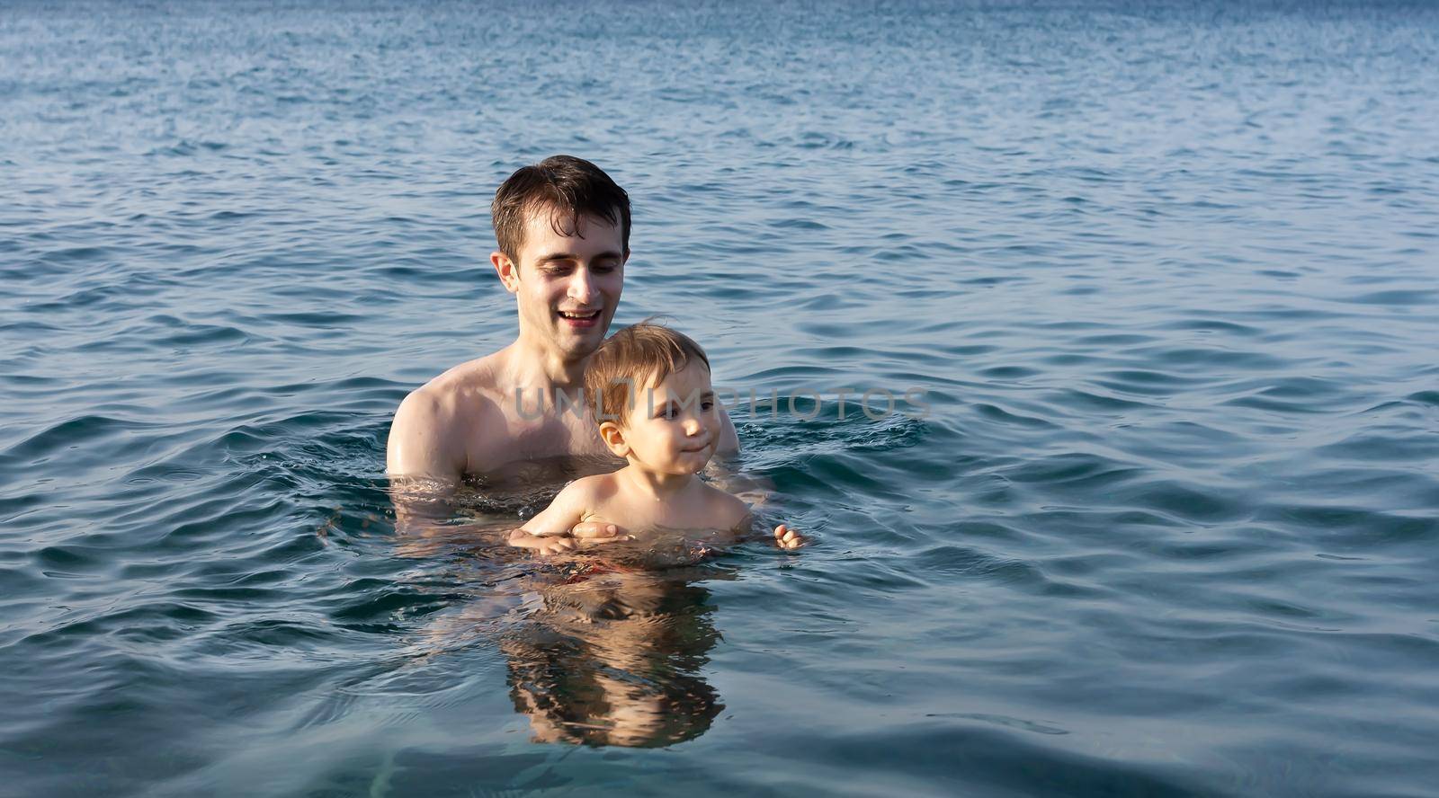 Happy family and healthy lifestyle. A young father teaches a child to swim in the sea