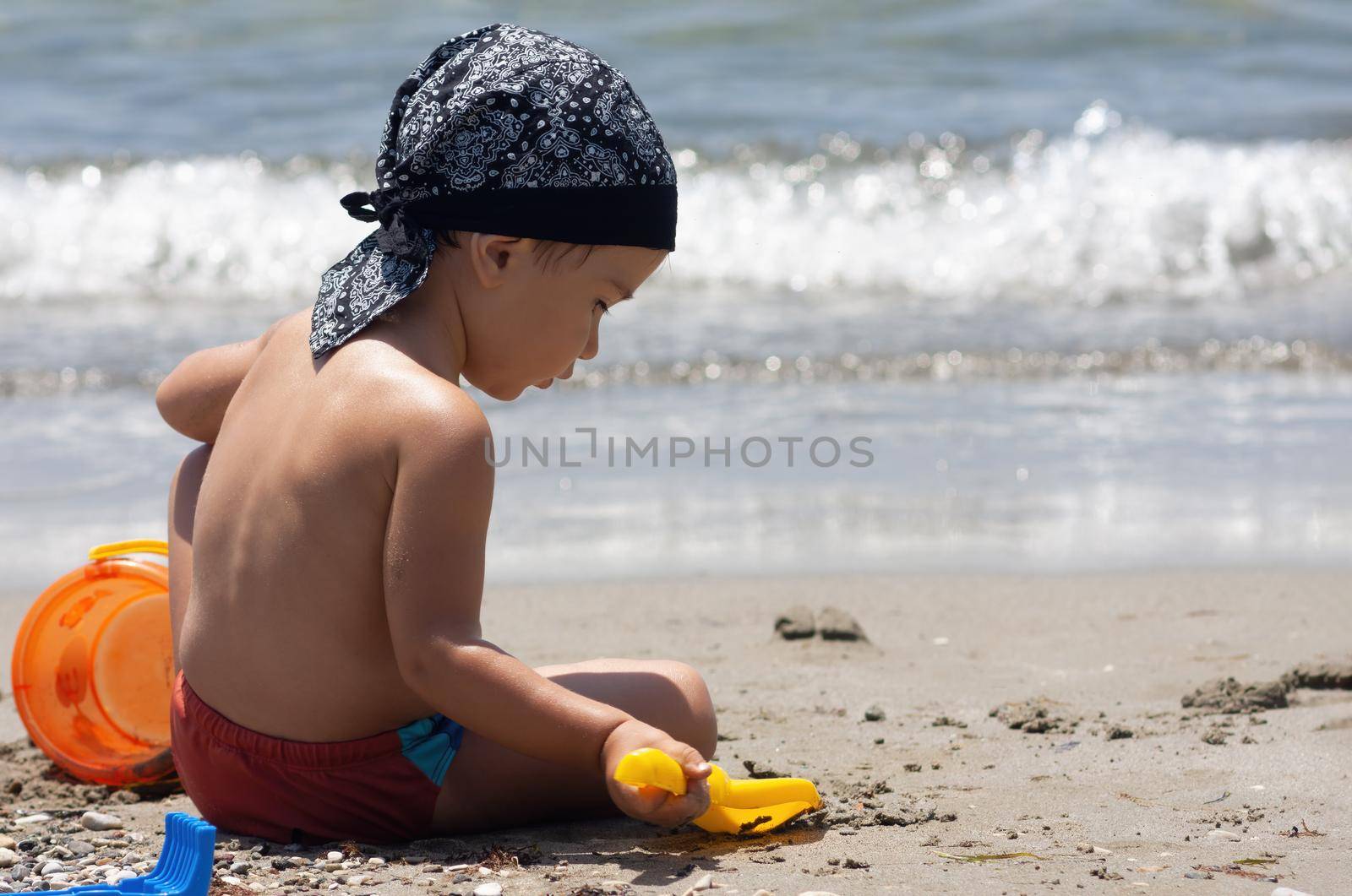 A little boy sits for the first time on the seashore enjoying the fresh air and sea waves