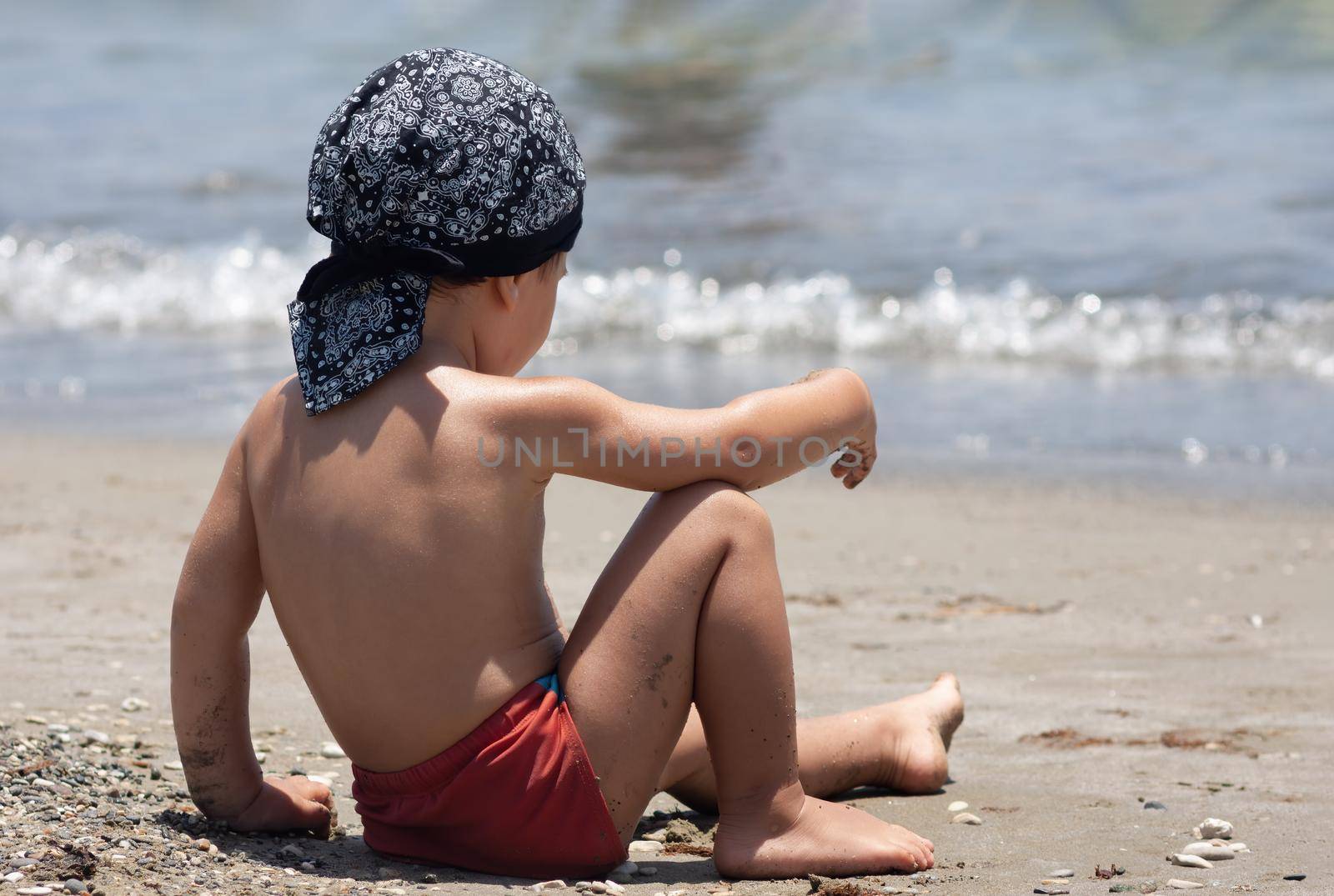 A little boy sits for the first time on the seashore enjoying the fresh air and sea waves