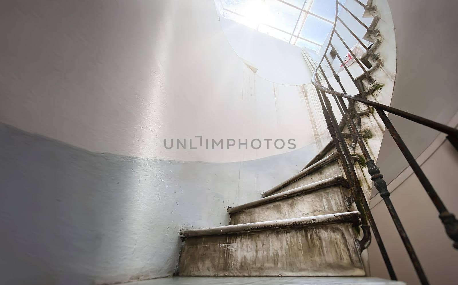 Ancient spiral staircase with marble steps and wrought iron handrail. Natural light coming in through the skylight. Architecture and circular shape