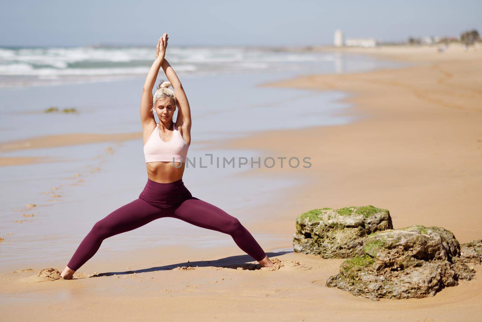 Caucasian blonde woman practicing yoga in the beach by javiindy