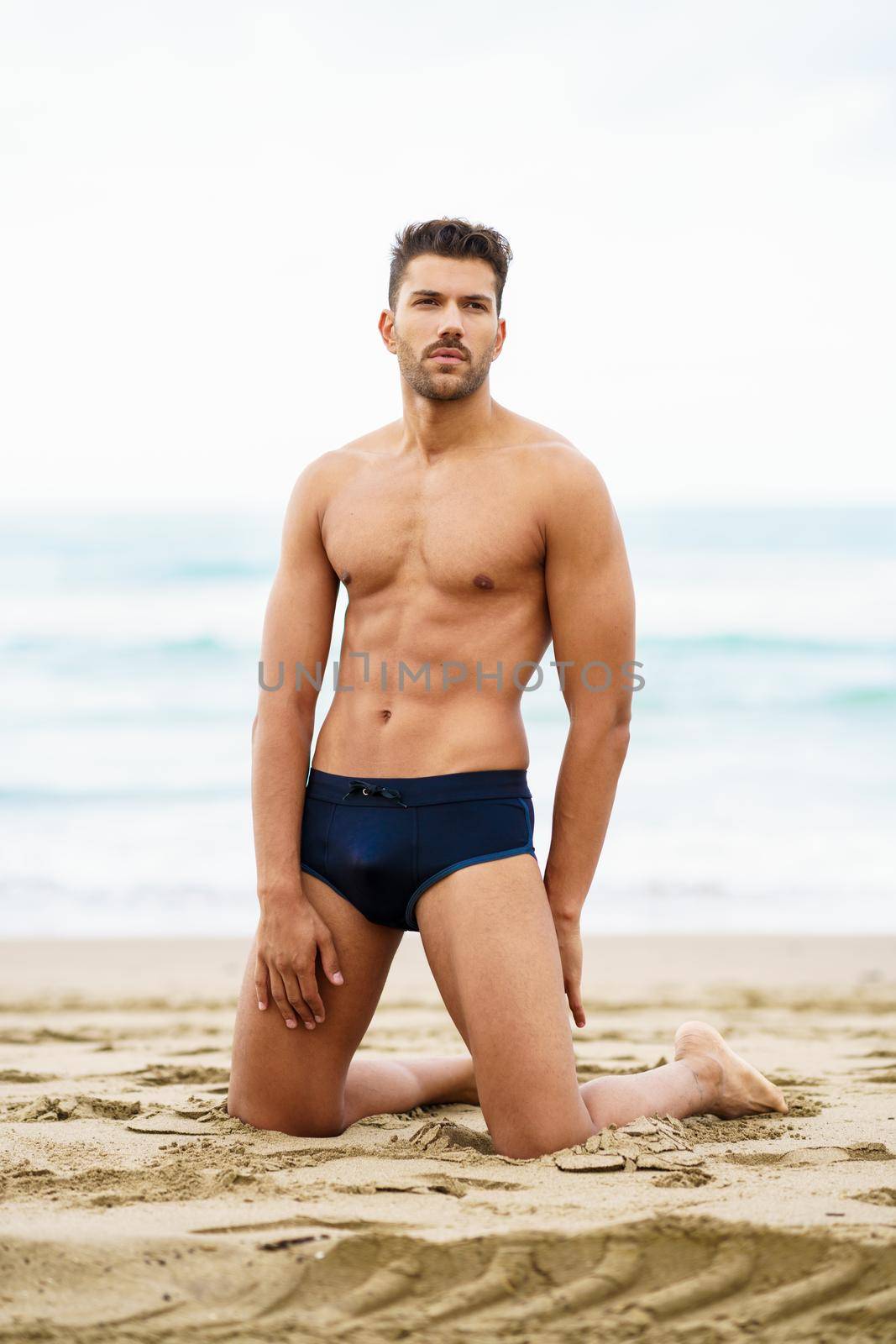 Handsome muscular man on his knees on the sand of the beach