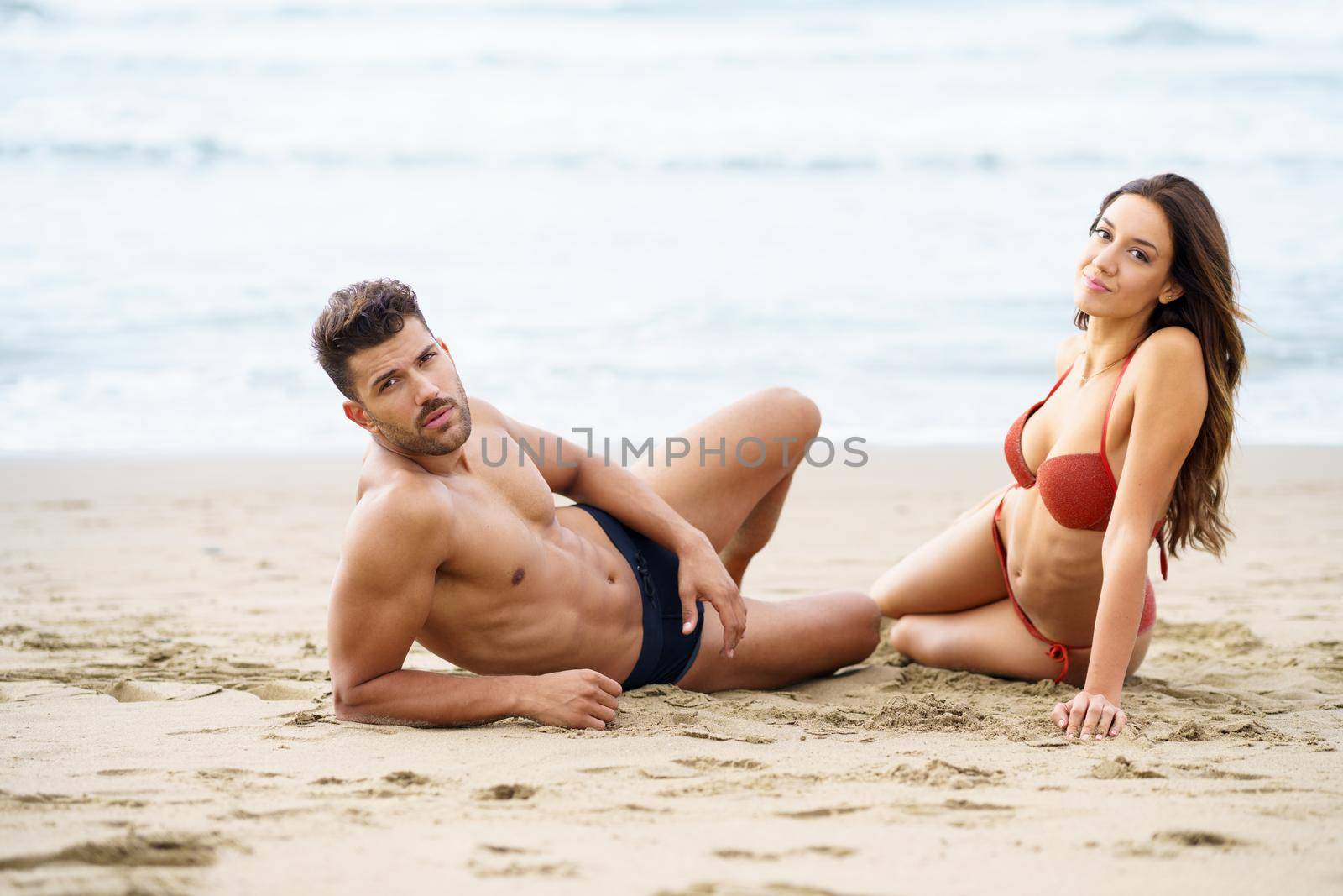 Young couple sitting together on the sand of the beach by javiindy