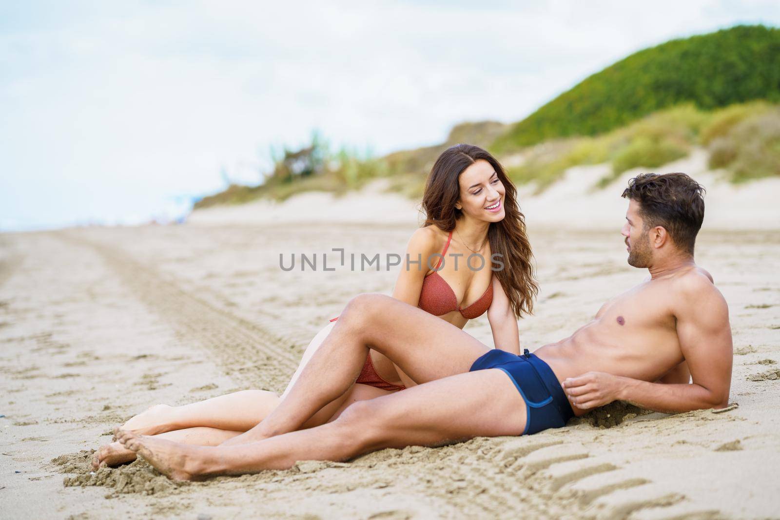 Young couple sitting together on the sand of the beach by javiindy