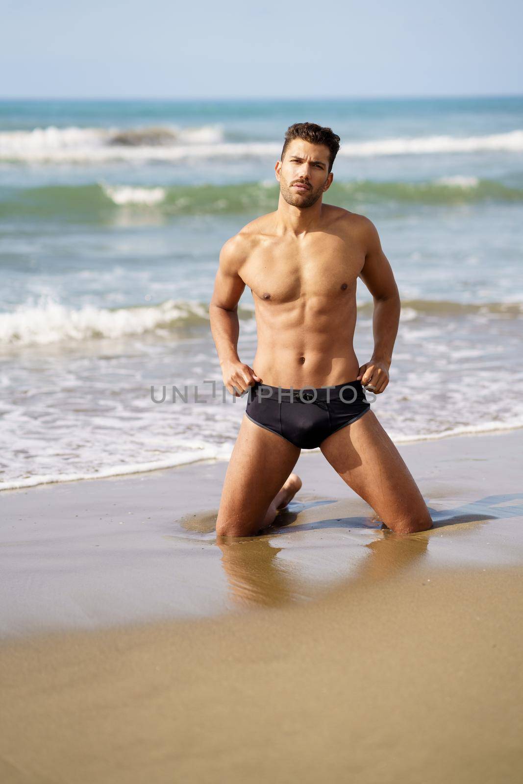 Handsome man on his knees on the sand of the beach by javiindy