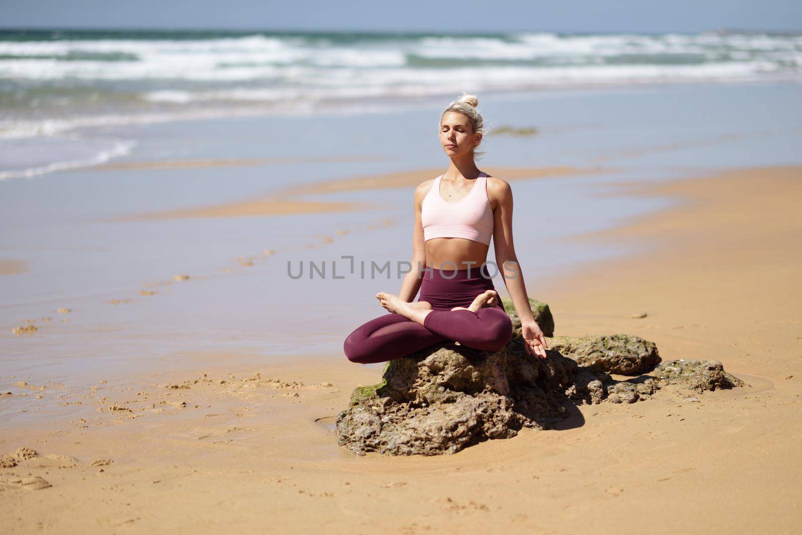 Caucasian blonde woman practicing yoga in the beach by javiindy