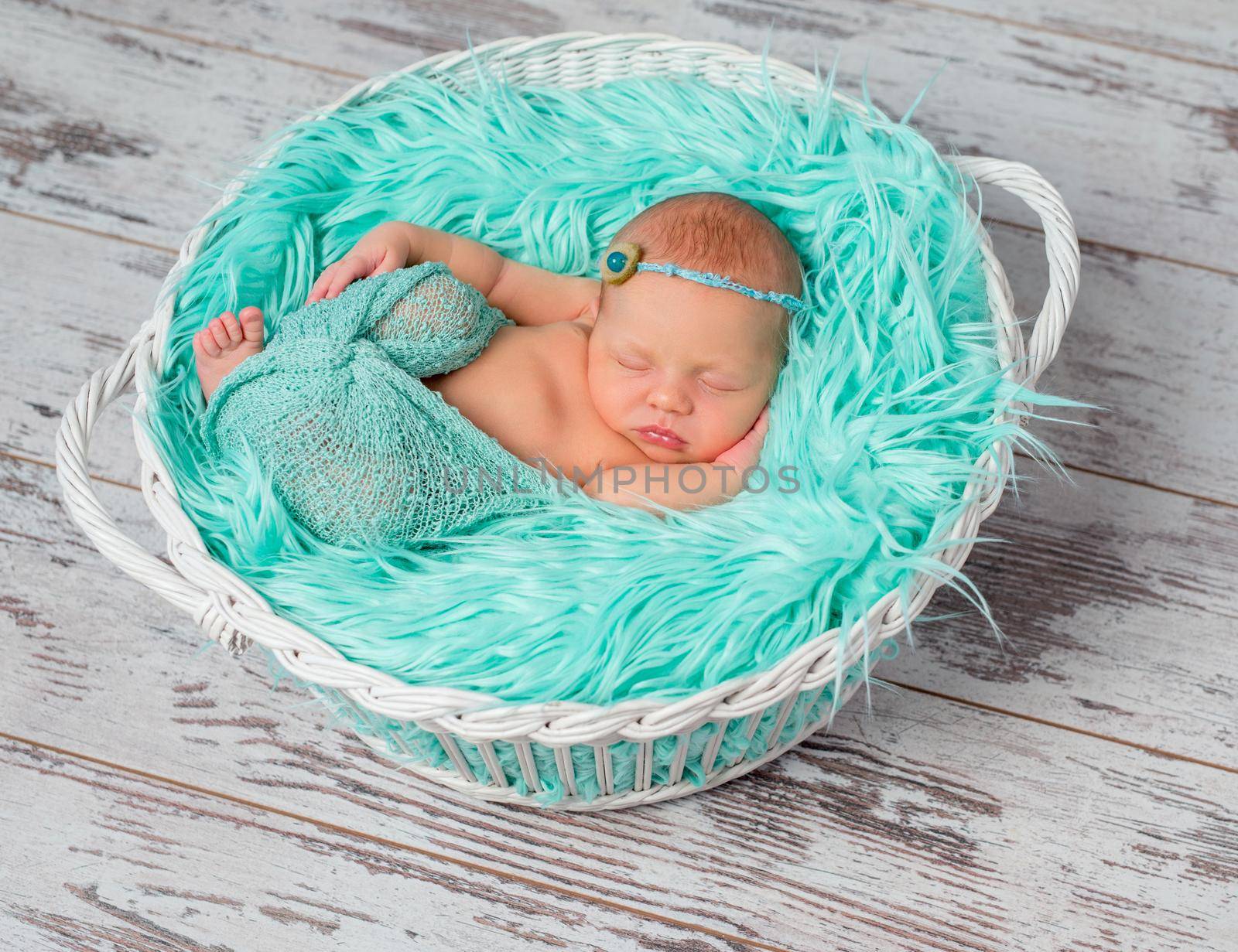 lovely sleeping newborn girl in round cot with turquoise fluffy blanket