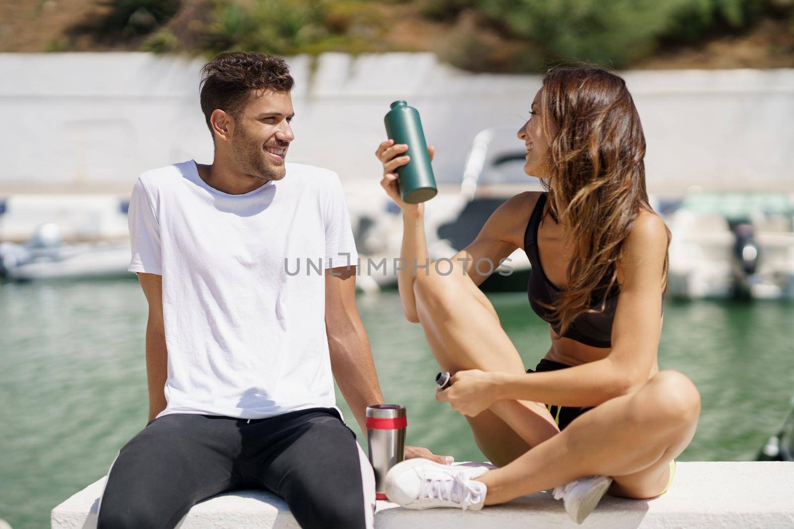 Young fitness people hydrate themselves with water in metal bottles while taking a break after sport.