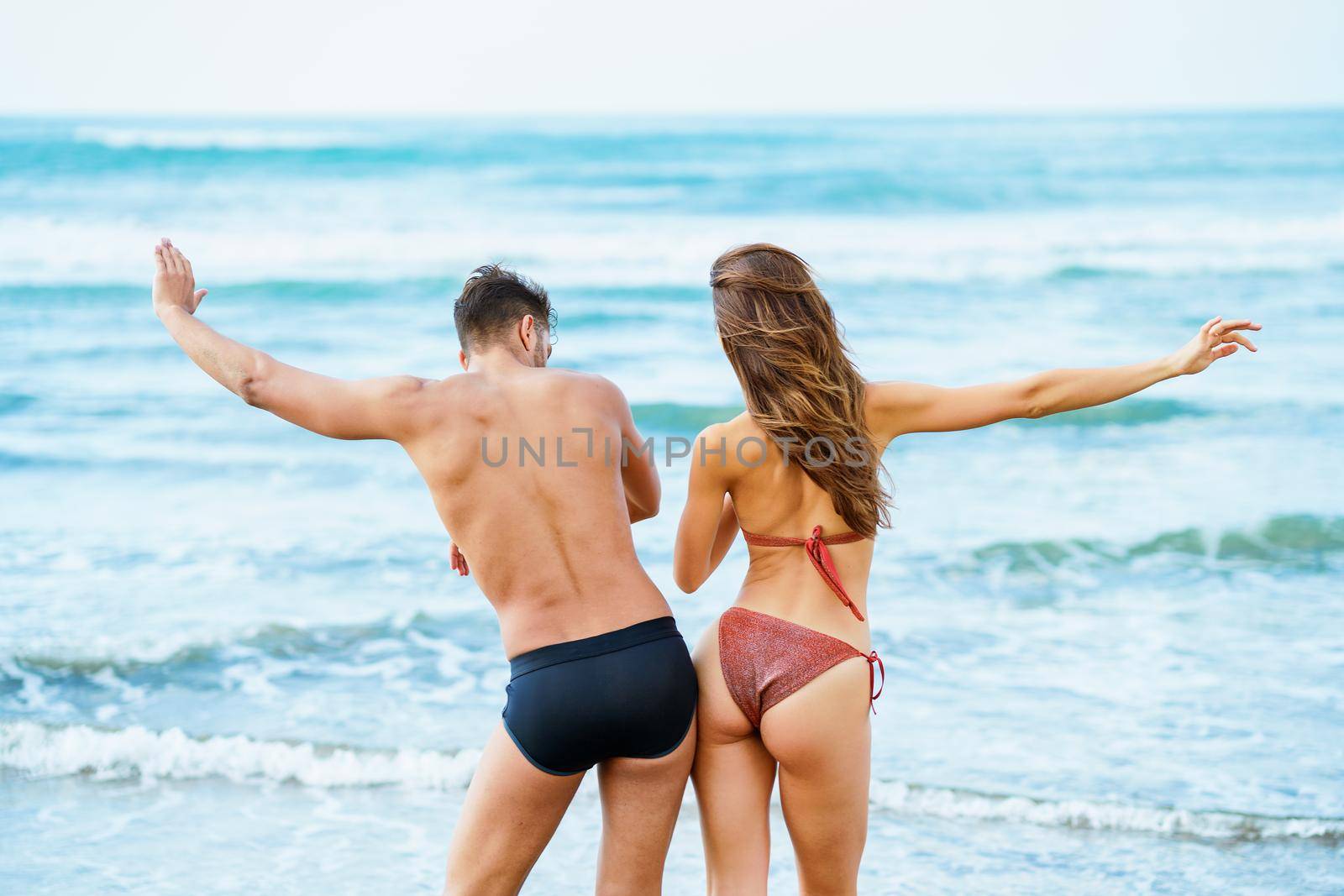 Rear view of a young couple with beautiful bodies in swimwear having fun on a tropical beach