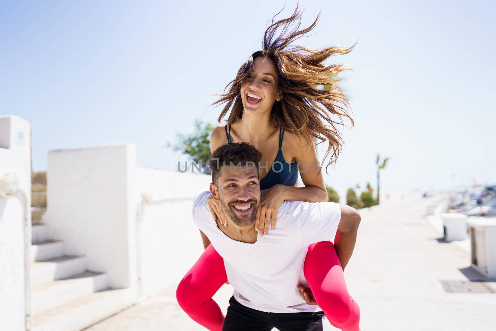 Man carrying his girlfriend on piggyback wearing sportswear. Couple having fun together.