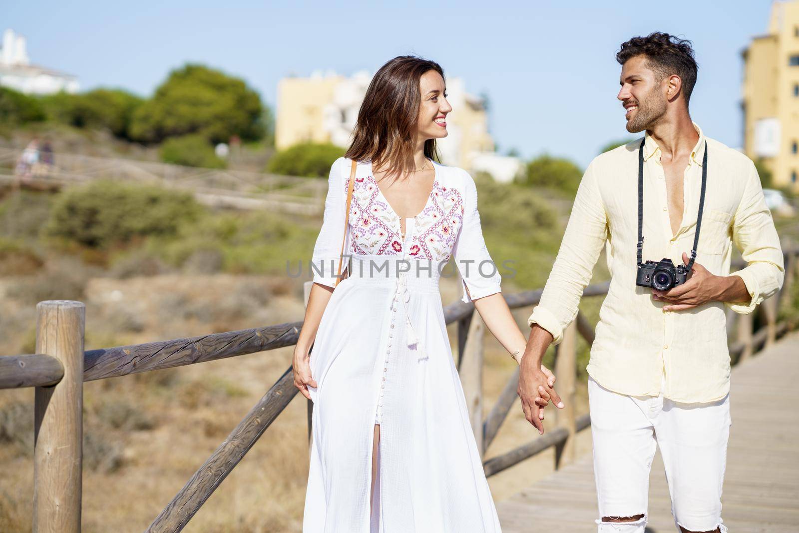 Happy loving couple walking along a wooden path towards the beach in a coastal area.