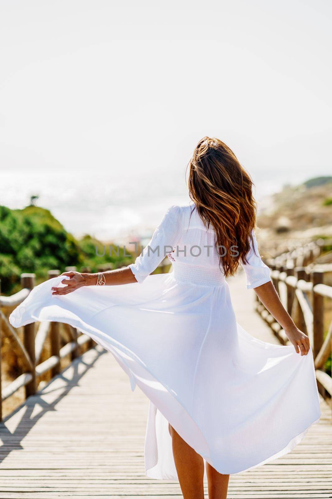 Young woman wearing a beautiful white dress in Spanish fashion on a boardwalk on the beach. by javiindy