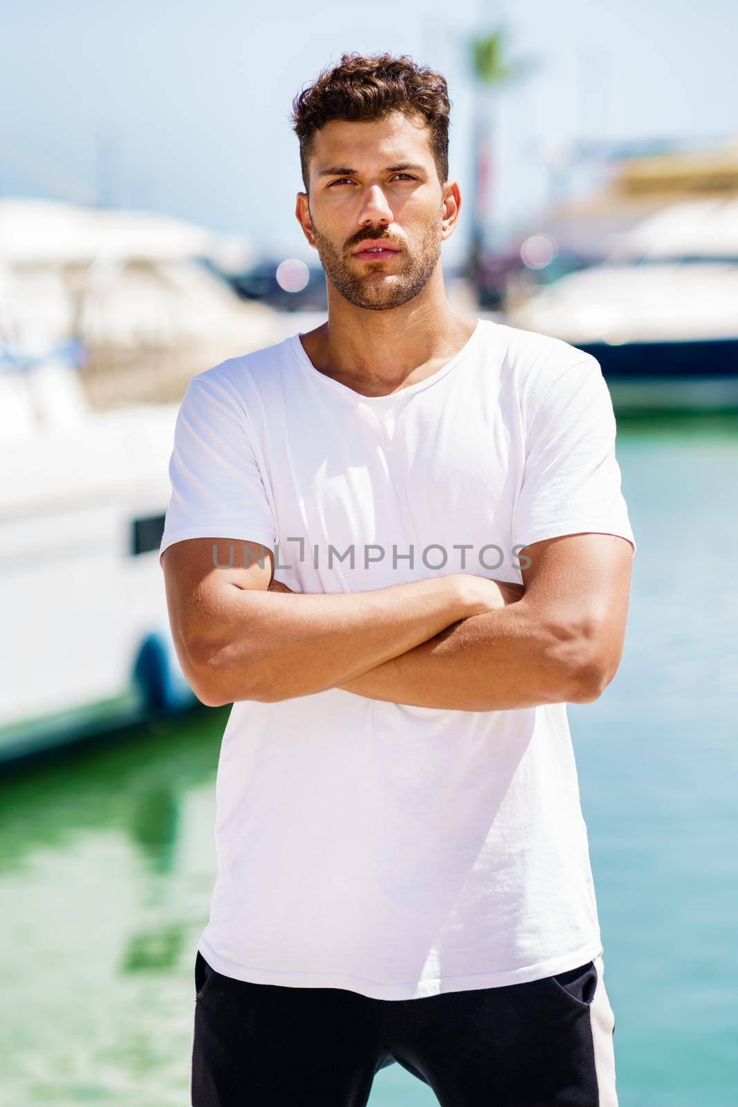 Fitness man, model of fashion, in sportswear outfit posing on waterfront harbour.