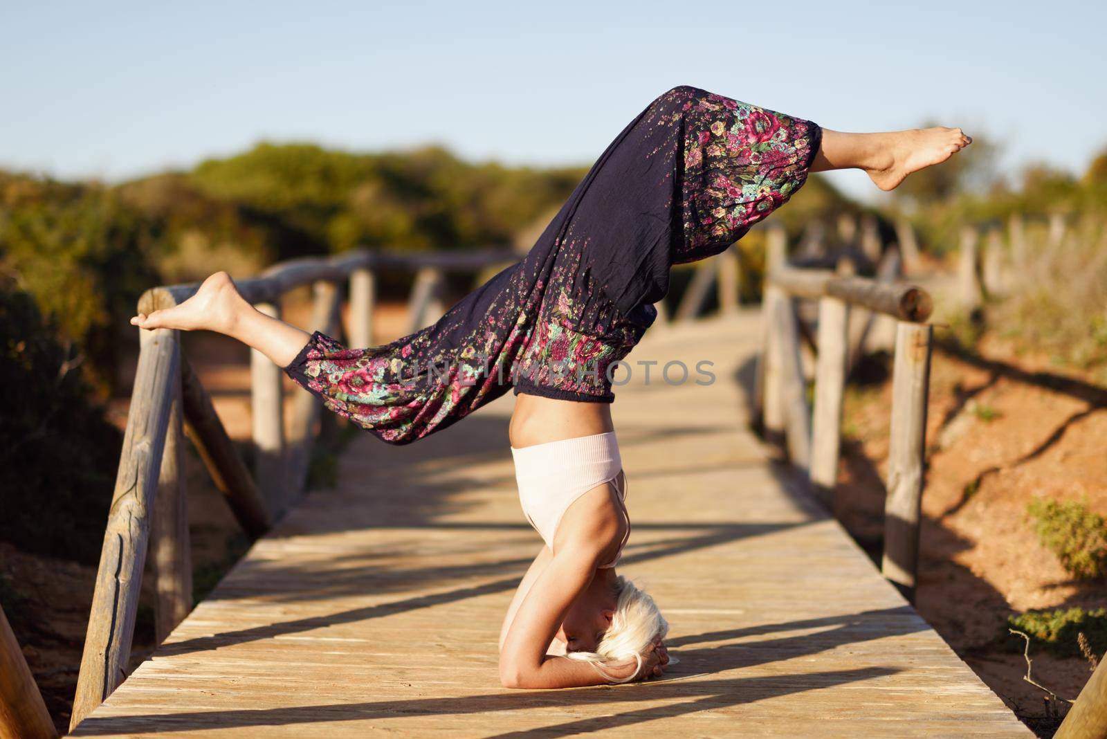 Woman enjoying the sunset on a beautiful beach in Cadiz, Andalusia, Spain. Caucasian female practicing yoga on wooden bridge.