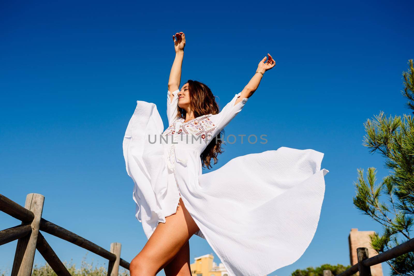 Young beautiful woman raising her arms in a beautiful white dress in Spanish fashion against a blue sky in nature