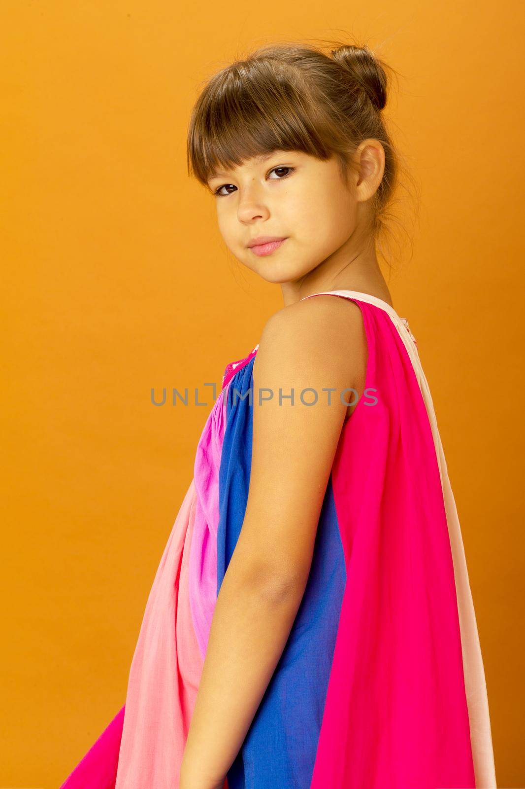 A close-up shot of a pretty teenage girl of ten. Beautiful girl in a bright summer dress posing on an isolated background. Portrait of a child looking at the camera with a serious facial expression