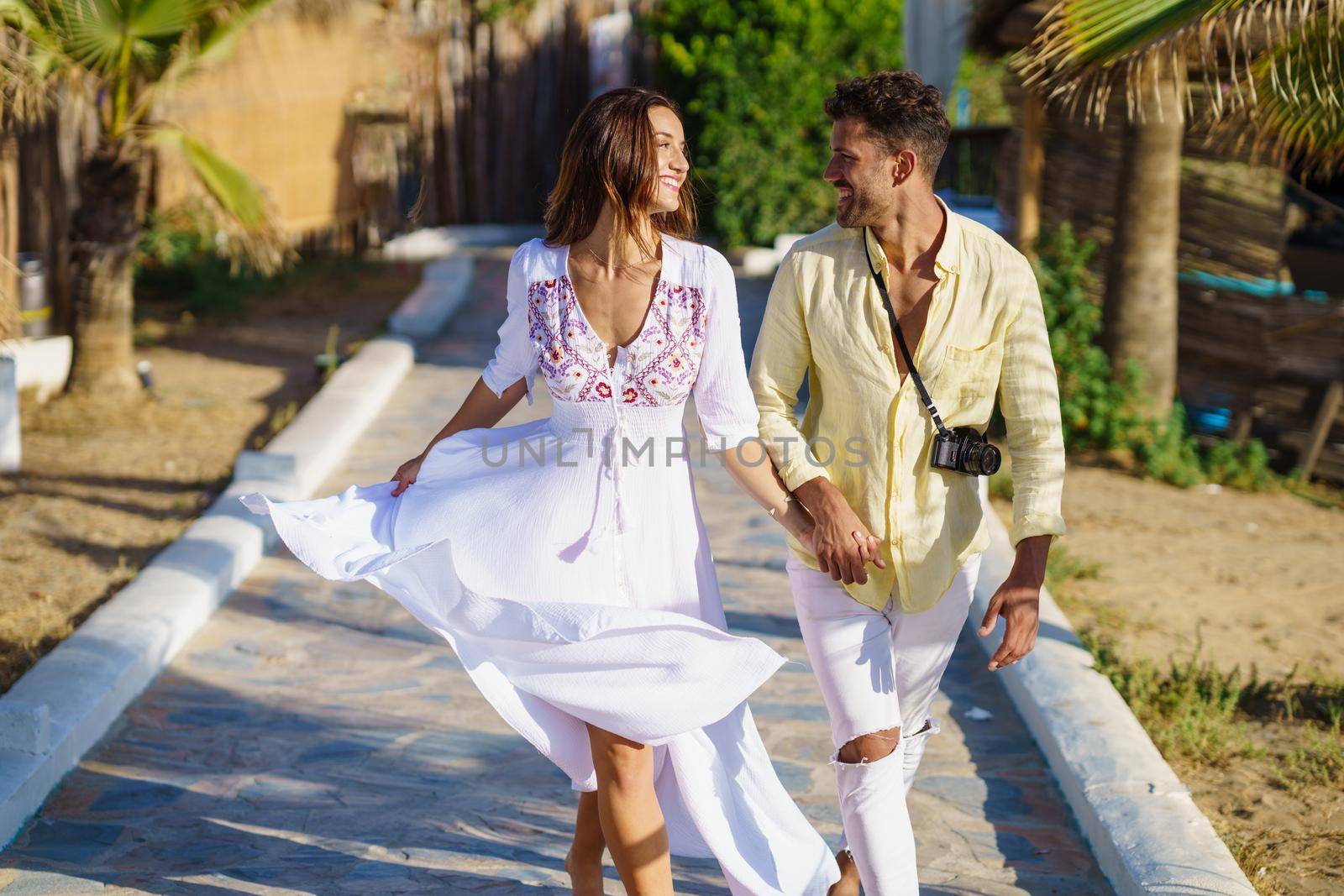 Happy loving couple walking along a wooden path towards the beach in a coastal area.