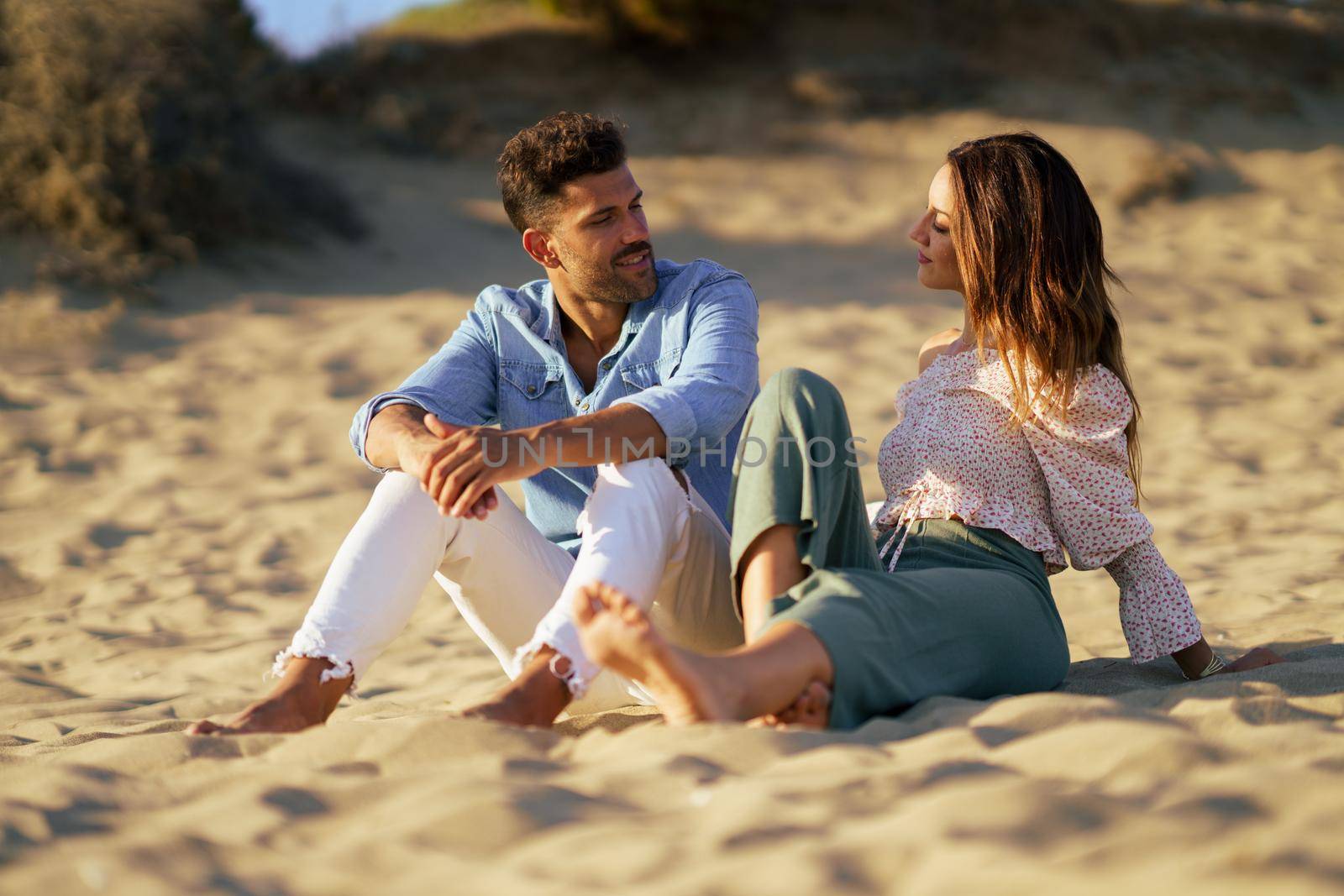 Attractive couple sitting on the sand of the beach by javiindy