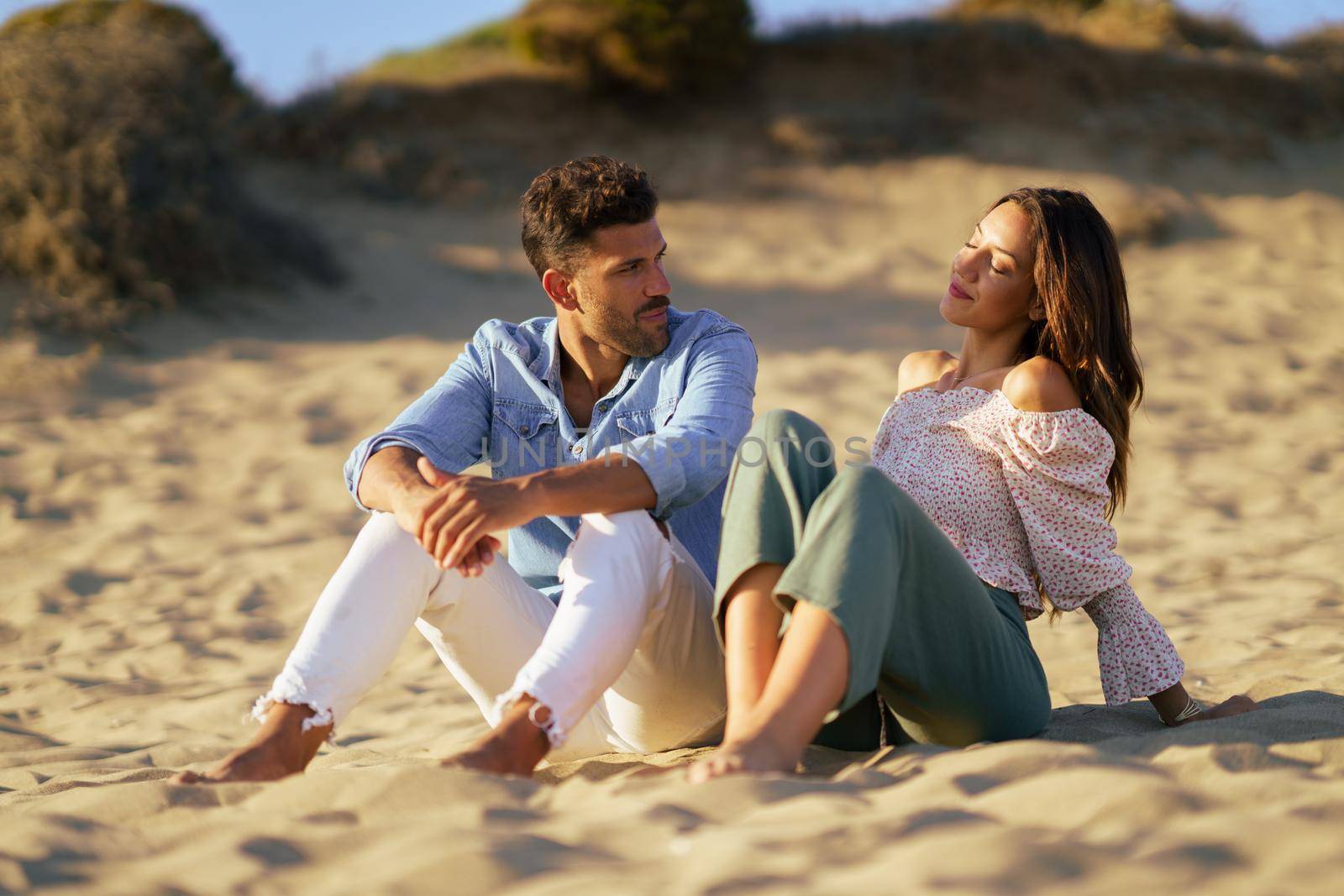 Attractive couple sitting on the sand of the beach by javiindy