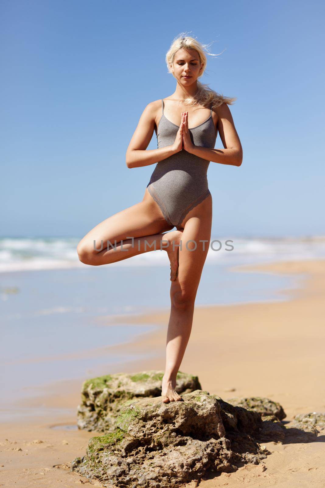 Caucasian woman practicing yoga at seashore. Young female standing on one leg while practicing the tree pose on a tranquil beach in Cadiz, Andalusia, Spain.