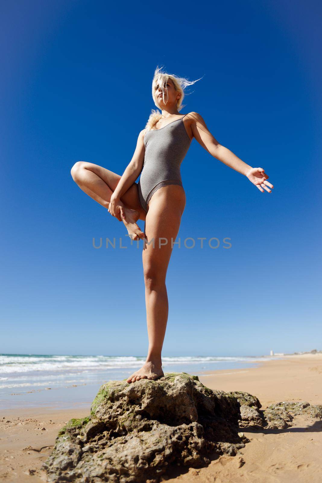 Caucasian woman practicing yoga at seashore. Young female standing on one leg while practicing the tree pose on a tranquil beach in Cadiz, Andalusia, Spain.